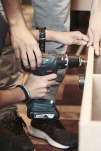 Un animateur aide un jeune menuisier à utilser une perceuse